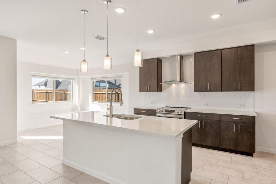 Kitchen with large white island, dark wood cabinets, stainless steel range, and pendant lights over tile floors