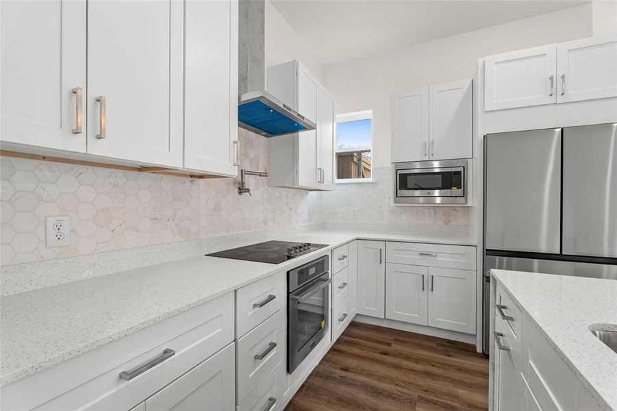 Kitchen featuring light stone countertops, wall chimney exhaust hood, white cabinetry, appliances with stainless steel finishes, and backsplash Kitchen featuring light stone countertops, wall chimney exhaust hood, white cabinetry, appliances with stainless steel finishes, and backsplash