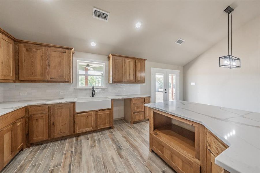 Kitchen featuring brown cabinets, french doors, light stone countertops, vaulted ceiling, and wood finish floors Kitchen featuring brown cabinets, french doors, light stone countertops, vaulted ceiling, and wood finish floors