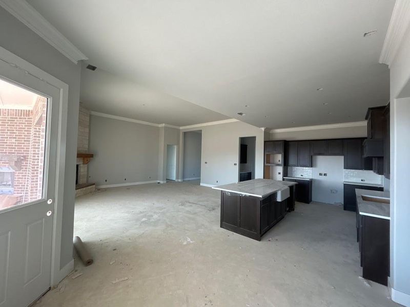 Kitchen with a kitchen island, ornamental molding, a fireplace, light countertops, and unfinished concrete floors