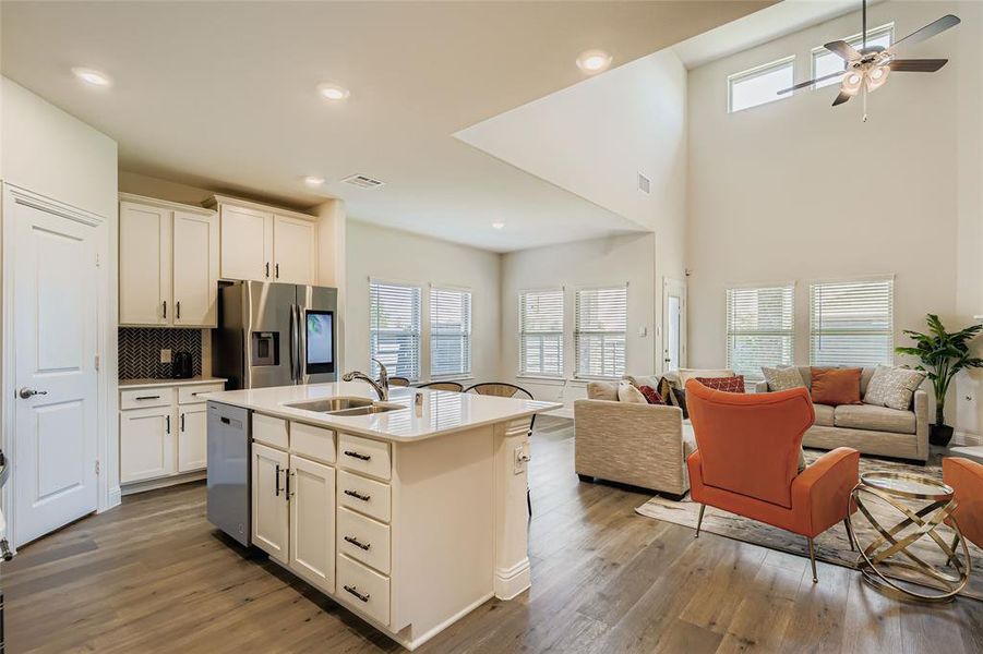 Kitchen featuring open floor plan, appliances with stainless steel finishes, a kitchen island with sink, decorative backsplash, and white cabinets