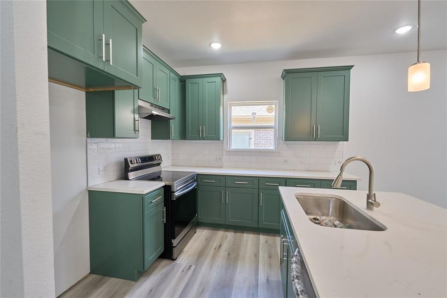 Kitchen featuring green shaker-style cabinetry, white countertops, wood-finish flooring, a stainless steel sink with a gooseneck faucet, and white subway tile backsplash