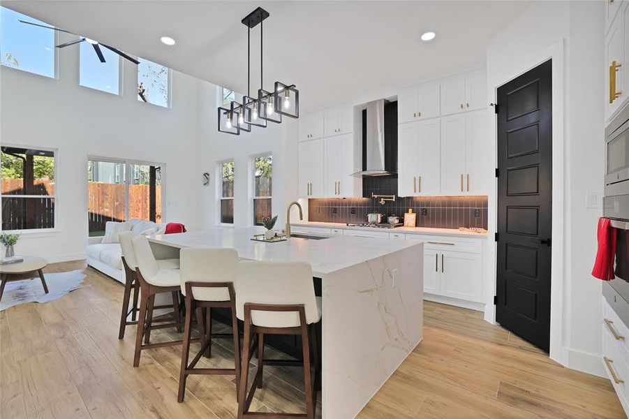 Kitchen with wall chimney range hood, decorative backsplash, white cabinetry, light wood-style flooring, and recessed lighting