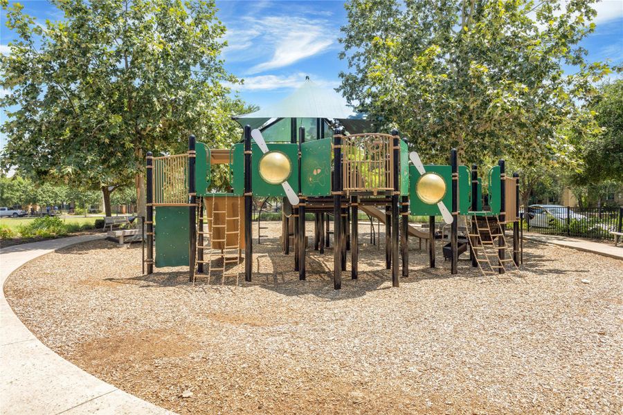 A well-maintained community playground awaits, featuring varied play structures over soft wood chips.