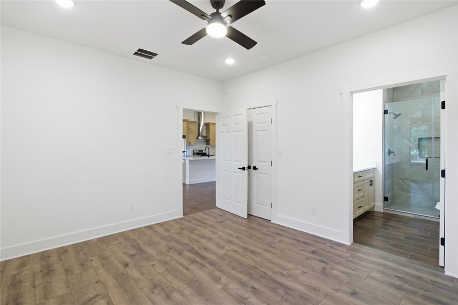A well-lit room showcasing rich hardwood flooring, a ceiling fan, and seamless transitions to a contemporary kitchen and a modern bathroom. A well-lit room showcasing rich hardwood flooring, a ceiling fan, and seamless transitions to a contemporary kitchen and a modern bathroom.