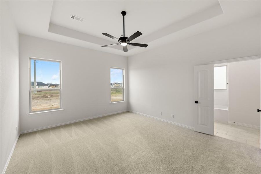 Unfurnished room with light colored carpet, a ceiling fan, and a tray ceiling