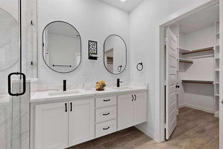 Full bathroom featuring wood finish floors, double vanity, a spacious closet, and a shower stall Full bathroom featuring wood finish floors, double vanity, a spacious closet, and a shower stall