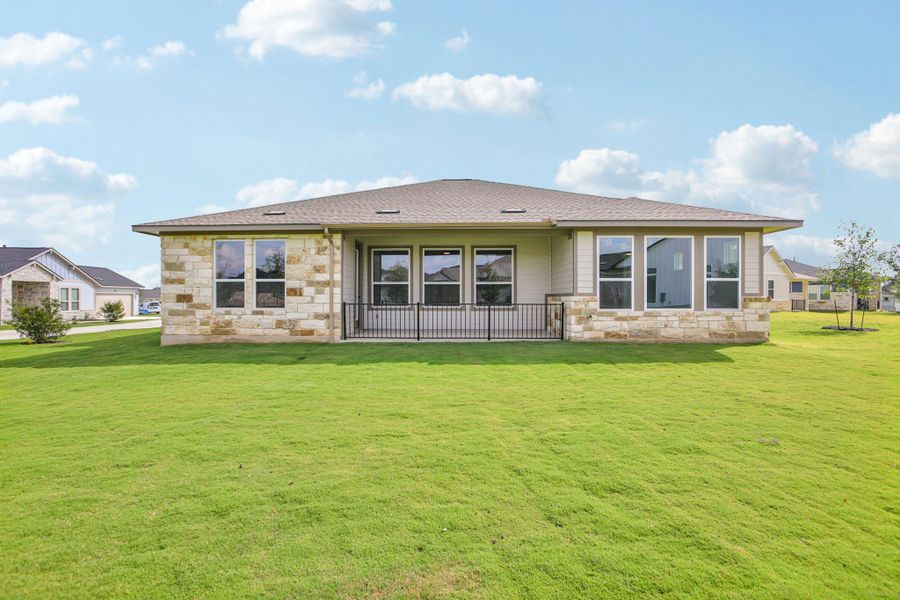 Rear view of house featuring stone siding, a lawn, a patio area, and a shingled roof