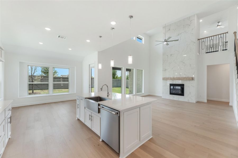 Open-concept kitchen with center island, farmhouse sink, and floor-to-ceiling marble fireplace in living area with high ceilings and hardwood floors