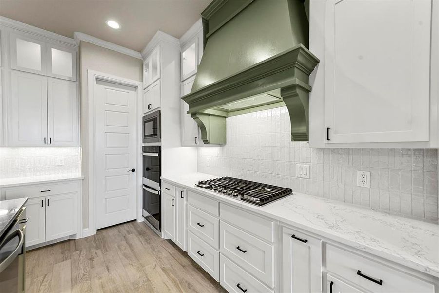 Kitchen featuring premium range hood, decorative backsplash, light hardwood / wood-style floors, white cabinetry, and stainless steel appliances