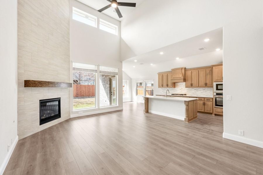 Open living area with tile fireplace and high ceilings flowing into kitchen with wood cabinets and center island Open living area with tile fireplace and high ceilings flowing into kitchen with wood cabinets and center island