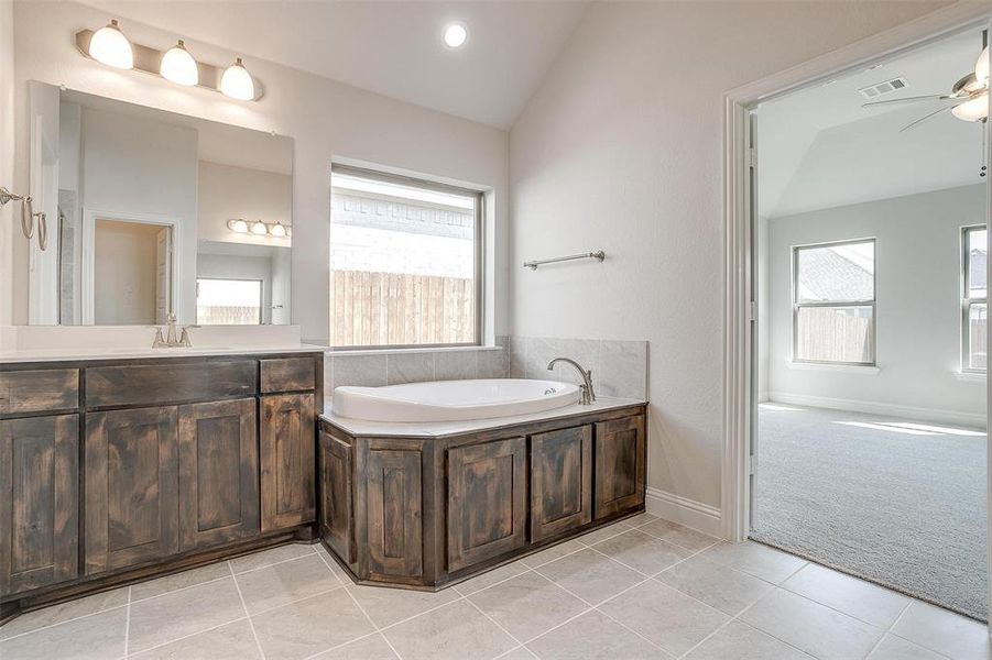 Bathroom with a wealth of natural light, lofted ceiling, a bath, and vanity