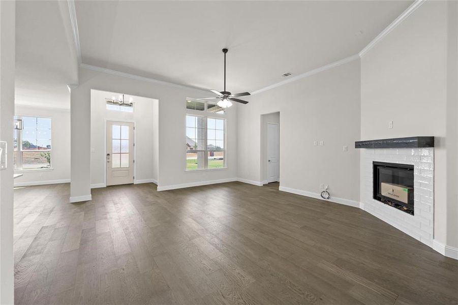 Unfurnished living room featuring ceiling fan with notable chandelier, a fireplace, dark hardwood / wood-style flooring, and a wealth of natural light