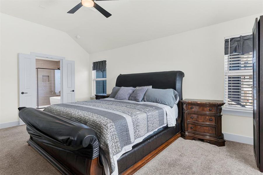 Bedroom featuring vaulted ceiling, a ceiling fan, ensuite bathroom, and light colored carpet Bedroom featuring vaulted ceiling, a ceiling fan, ensuite bathroom, and light colored carpet