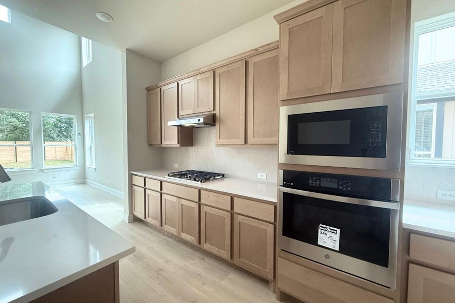 Kitchen featuring light wood-finish cabinetry, light countertops, a built-in stainless steel microwave, a built-in stainless steel oven, and a gas cooktop Kitchen featuring light wood-finish cabinetry, light countertops, a built-in stainless steel microwave, a built-in stainless steel oven, and a gas cooktop