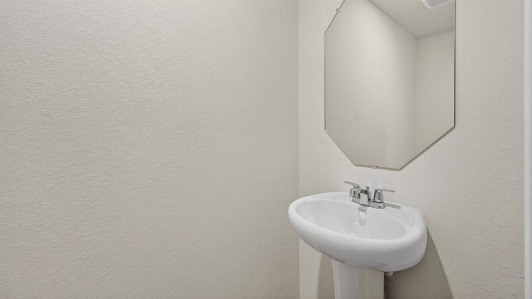 Pedestal sink with chrome faucet, complemented by a frameless octagonal mirror