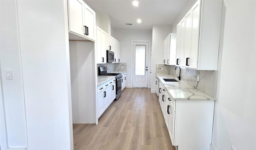 This kitchen features sleek white cabinetry with black handles, modern stainless steel appliances, and elegant countertops. The light flooring and ample natural light create a bright, inviting space.
