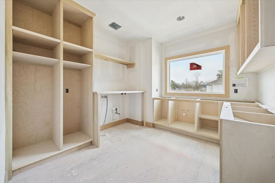 Second floor utility room designed with custom built cabinetry, open shelving, and space for a full size washer and dryer. Large window brings in natural light, making everyday tasks feel bright and organized.