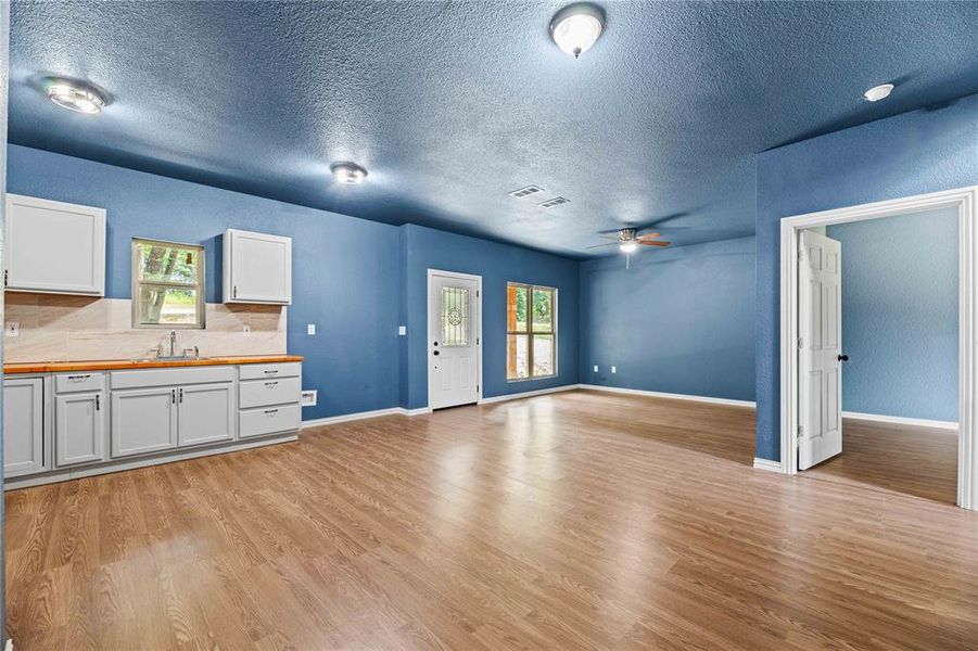 Unfurnished living room featuring a wealth of natural light, sink, light hardwood / wood-style flooring, and a textured ceiling Unfurnished living room featuring a wealth of natural light, sink, light hardwood / wood-style flooring, and a textured ceiling