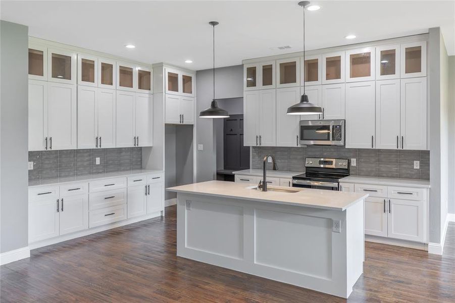 Kitchen featuring appliances with stainless steel finishes, glass insert cabinets, hanging light fixtures, tasteful backsplash, and dark wood finished floors Kitchen featuring appliances with stainless steel finishes, glass insert cabinets, hanging light fixtures, tasteful backsplash, and dark wood finished floors