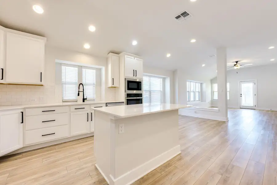 Kitchen with decorative backsplash, white cabinets, stainless steel oven, a center island, and open floor plan