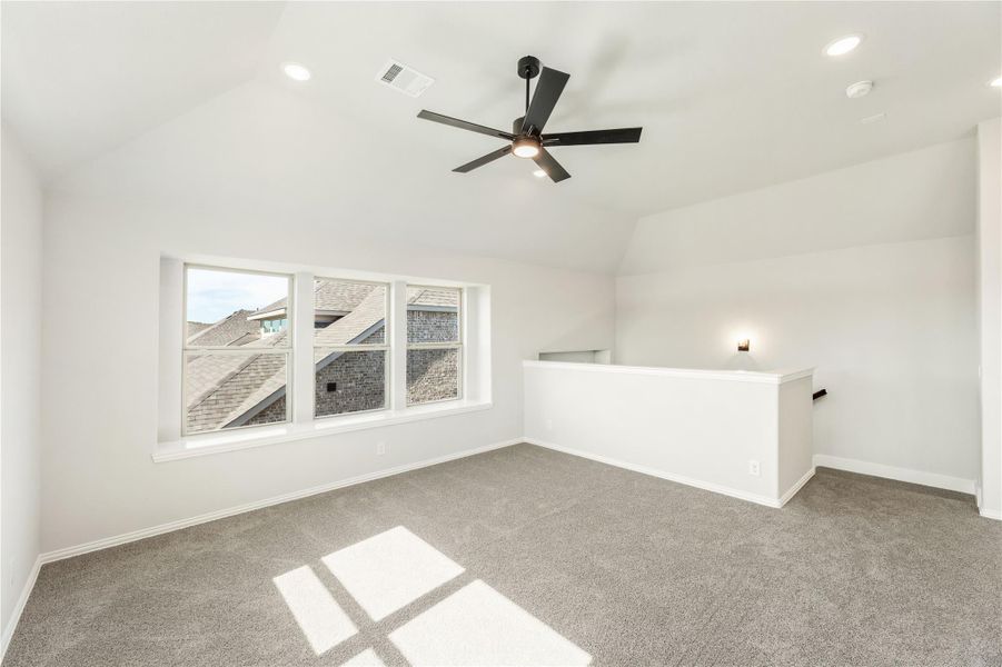 Open bonus room with vaulted ceiling, black ceiling fan, gray carpet, and large window overlooking neighboring rooftops