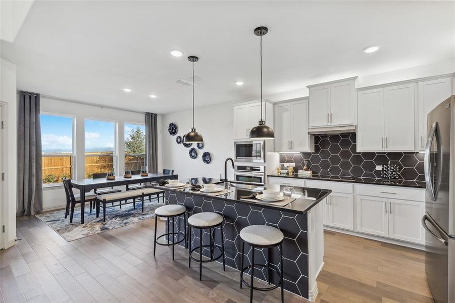 Kitchen with a breakfast bar, hanging light fixtures, an island with sink, stainless steel appliances, and white cabinets