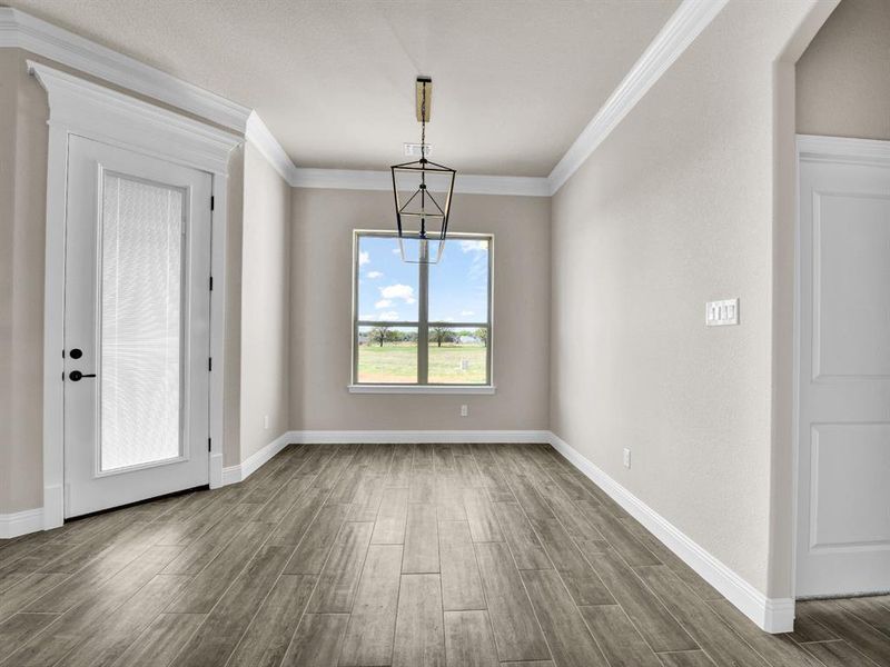 Unfurnished dining area with ornamental molding, baseboards, a notable chandelier, and wood tiled floor Unfurnished dining area with ornamental molding, baseboards, a notable chandelier, and wood tiled floor