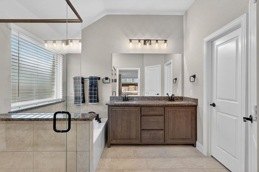 Spacious bathroom featuring a dual vanity with granite countertops, a built-in bathtub, a glass-enclosed shower, tile flooring, and a large window with blinds Spacious bathroom featuring a dual vanity with granite countertops, a built-in bathtub, a glass-enclosed shower, tile flooring, and a large window with blinds