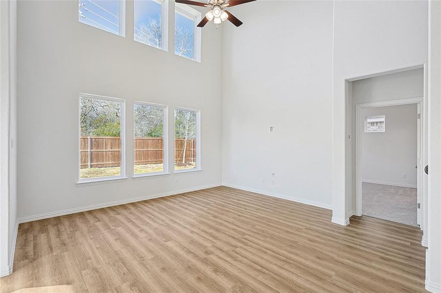 Unfurnished living room featuring ceiling fan, light wood-type flooring, and a towering ceiling