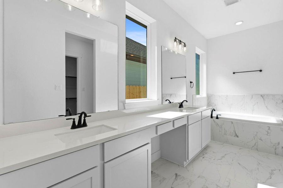 A dual vanity with ample counter space and elegant cabinetry provides plenty of room for two, with large mirrors and modern lighting that make the space feel bright and open.