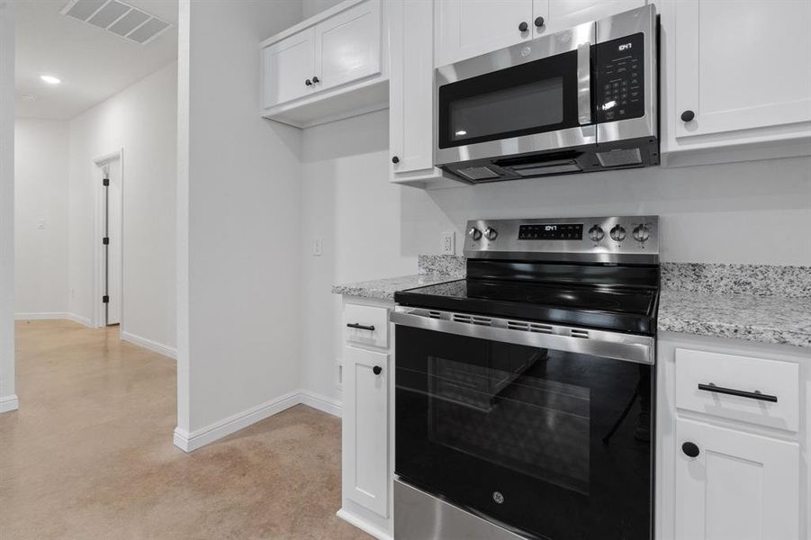 Kitchen with light granite countertops, appliances with stainless steel finishes, and white cabinetry