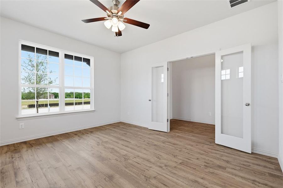 Spacious room with wood-finish flooring, a large multi-pane window, and a ceiling fan