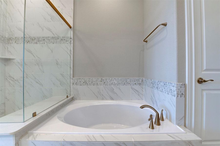 Primary bathroom featuring soaking tub with elegant tile surround and modern finishes.