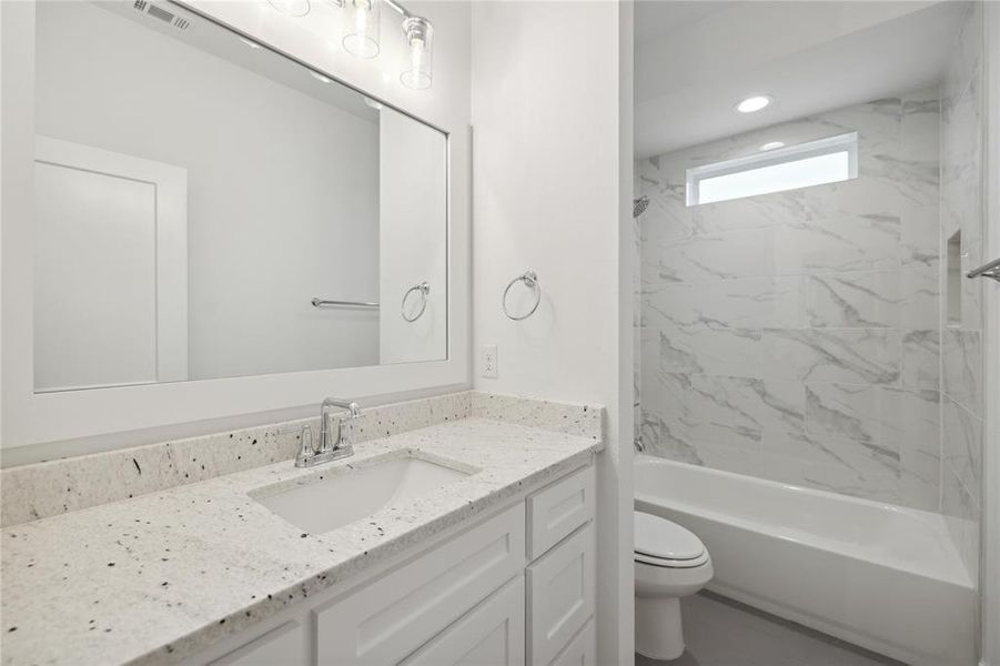 Full bathroom with tiled shower / bath combo, vanity, and toilet