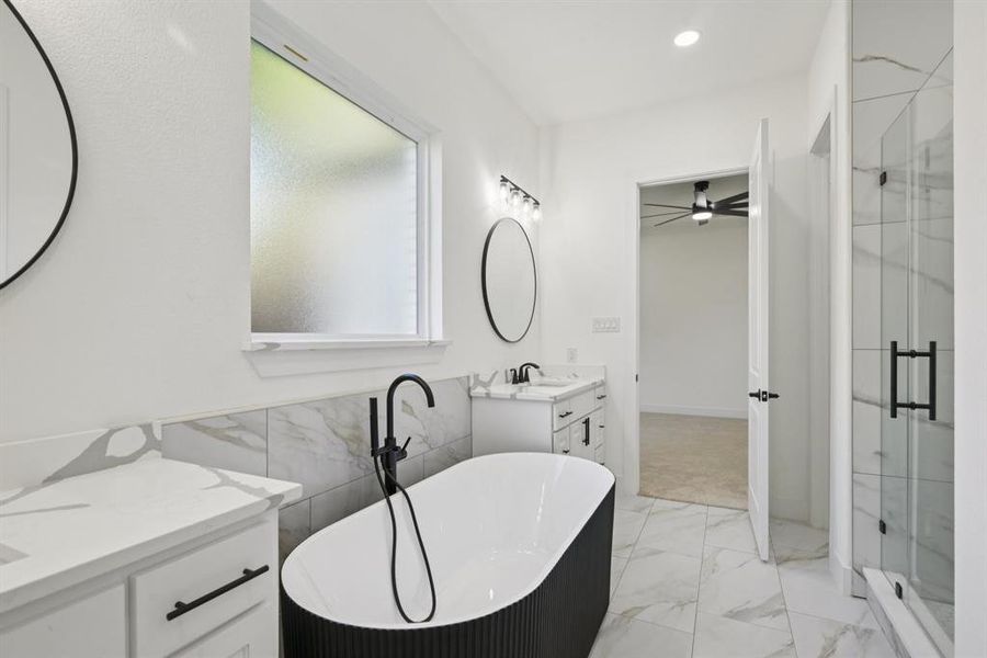 Bathroom featuring a freestanding tub, vanity, a shower stall, light marble finish floors, and tile walls