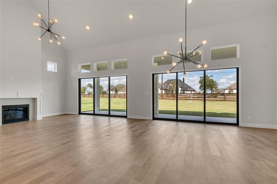 Unfurnished living room featuring an inviting chandelier, light hardwood / wood-style flooring, and a towering ceiling