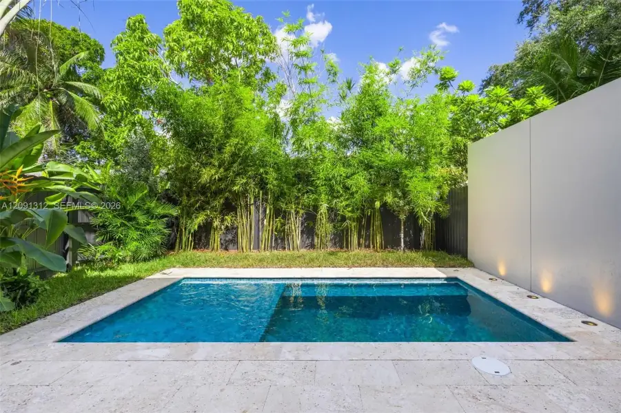 Swimming pool with natural stone decking, perimeter landscape screening, and integrated wall lighting Swimming pool with natural stone decking, perimeter landscape screening, and integrated wall lighting