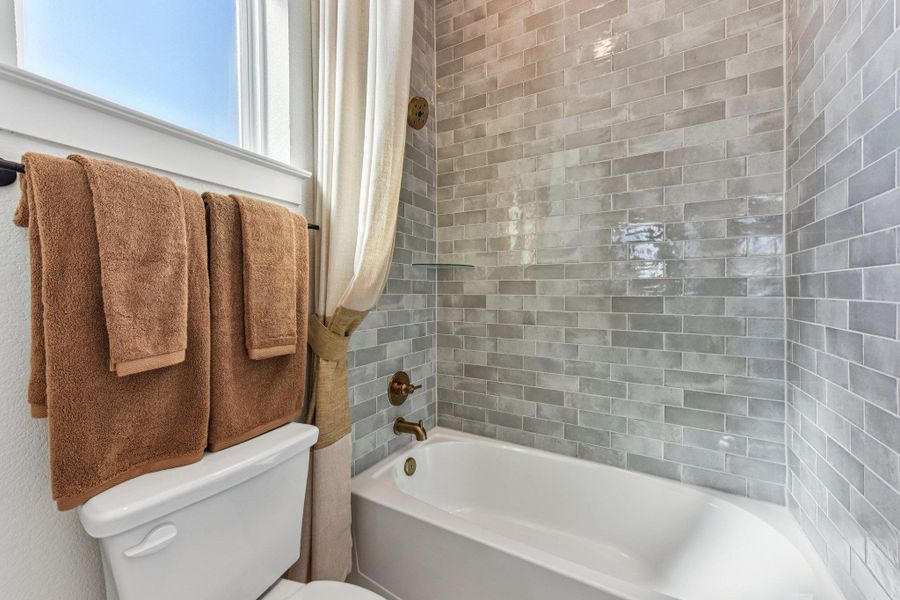 Glossy subway tile surrounds a deep soaking tub next to a bright window.