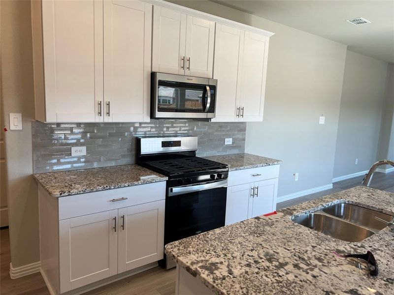 Kitchen featuring appliances with stainless steel finishes, white cabinetry, dark wood-style floors, tasteful backsplash, and light stone countertops