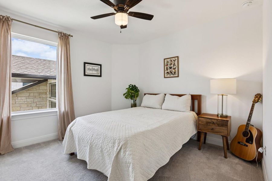 This inviting sleeping area features light-colored carpeting, a window with draperies, and a ceiling fan with integrated lighting