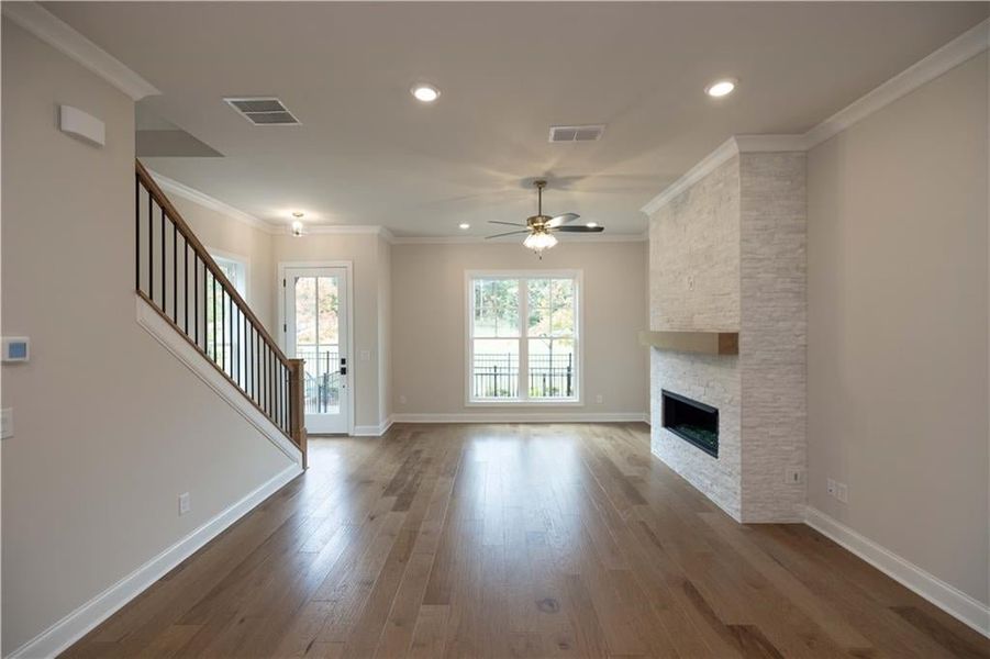 Unfurnished living room with ornamental molding, wood-type flooring, a fireplace, and ceiling fan