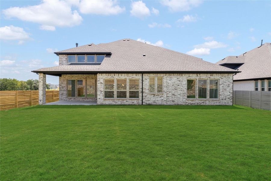 Rear exterior of two-story brick home with covered patio, large windows, and fenced backyard lawn