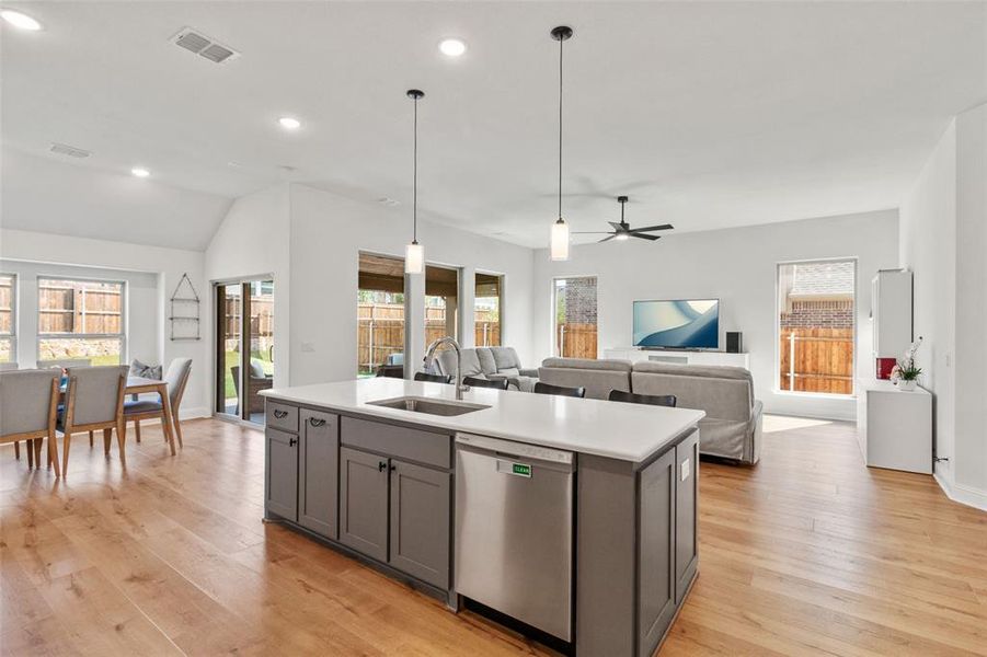 Kitchen featuring dishwasher, open floor plan, a center island with sink, light wood finished floors, and decorative light fixtures