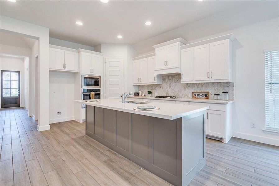 Contemporary kitchen featuring white cabinetry, light-colored countertops, a tile backsplash, and stainless steel appliances