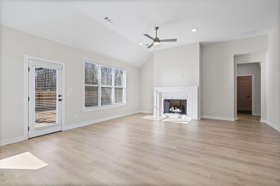 Unfurnished living room with a high end fireplace, vaulted ceiling, ceiling fan, light wood-style floors, and recessed lighting Unfurnished living room with a high end fireplace, vaulted ceiling, ceiling fan, light wood-style floors, and recessed lighting