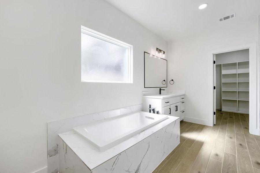 Indulge in a tranquil retreat with a deep soaking tub and stylish vanity in this bright bathroom.