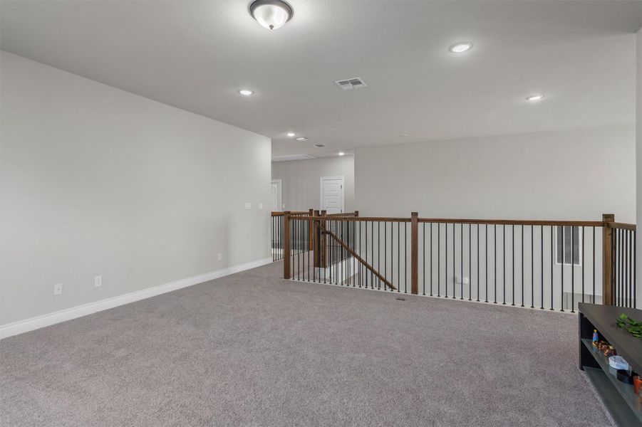 An open upper-level loft overlooks the staircase with plush carpeting and modern iron railing.
