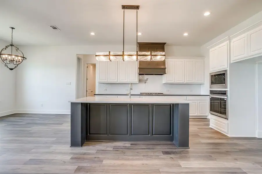 Kitchen featuring stainless steel appliances, a chandelier, a kitchen island with sink, light wood-style floors, and two tone cabinetry Kitchen featuring stainless steel appliances, a chandelier, a kitchen island with sink, light wood-style floors, and two tone cabinetry
