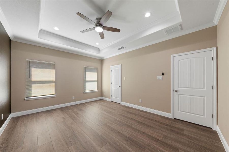 Spare room with wood finished floors, visible vents, baseboards, a tray ceiling, and crown molding